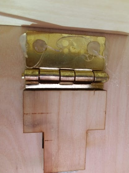 Metal hinge hot glued to the top of the dispensing area and the top side of the dispensing door